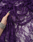 Hand holding deep eggplant purple floral stretch lace fabric showing soft texture