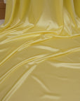 Close-up of yellow fabric with a hand holding it, with a glittery object in the background.