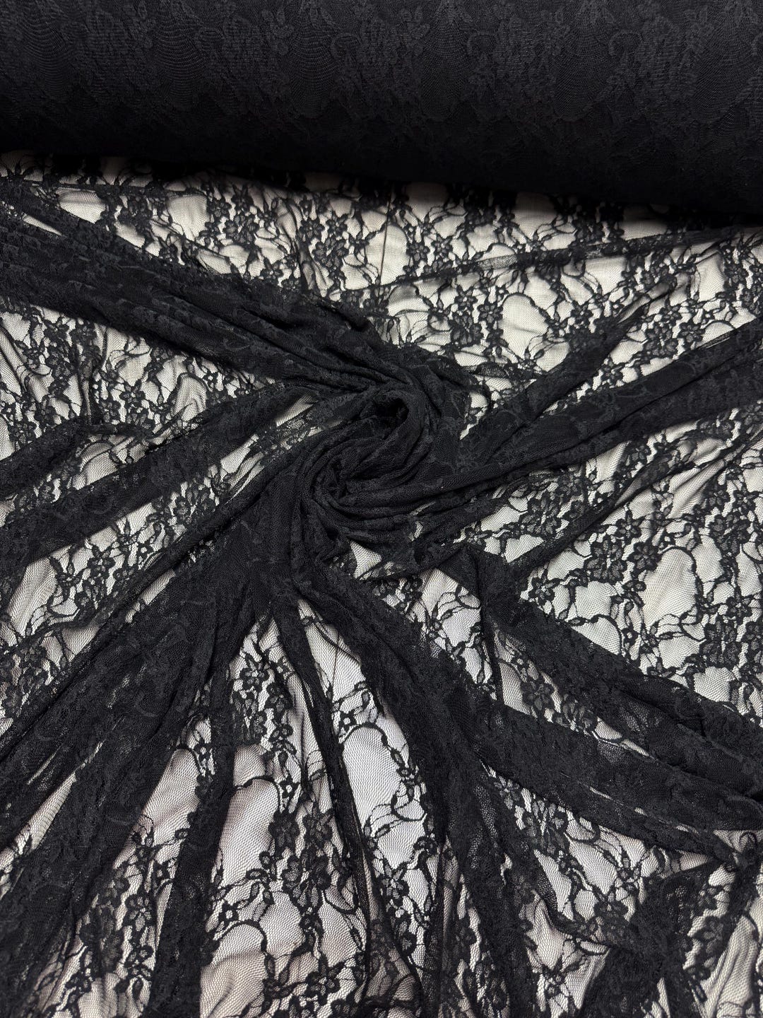 Black floral lace fabric draped showing intricate floral pattern