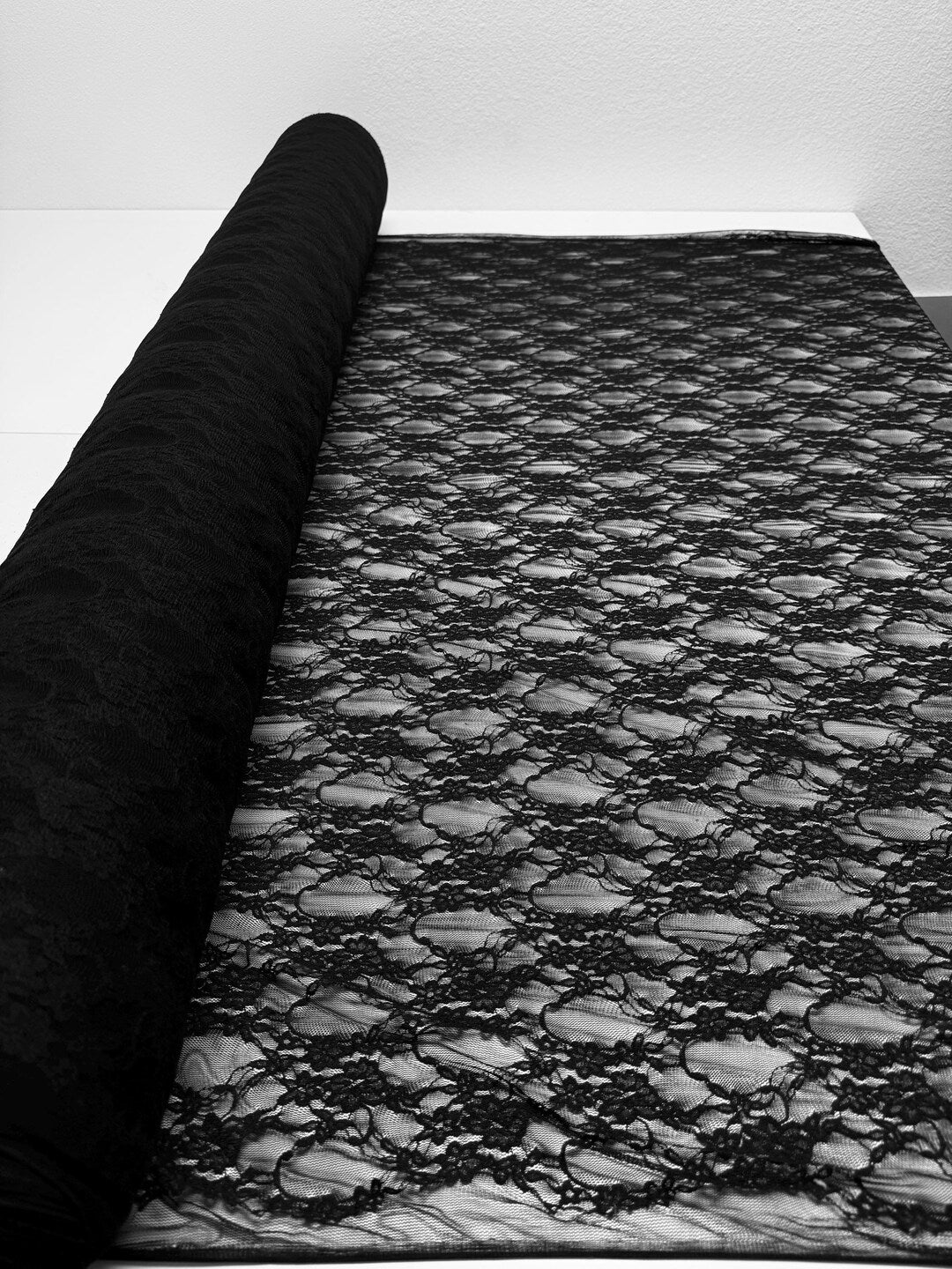 Black floral stretch lace fabric roll partially unrolled showing detailed floral pattern