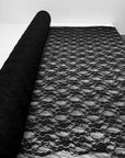 Black floral stretch lace fabric roll partially unrolled showing detailed floral pattern