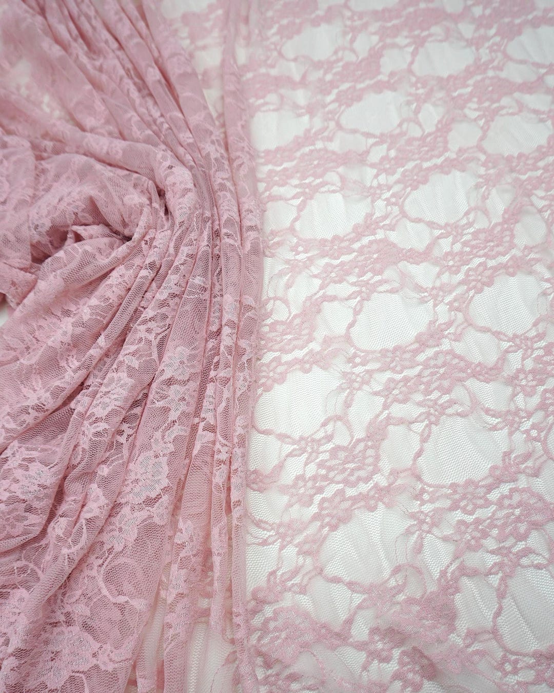 Blush pink floral stretch lace fabric draped and folded showing intricate pattern