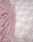 Blush pink floral stretch lace fabric draped and folded showing intricate pattern