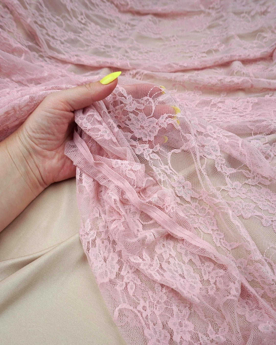 Blush pink floral stretch lace fabric held up close-up showing intricate detail