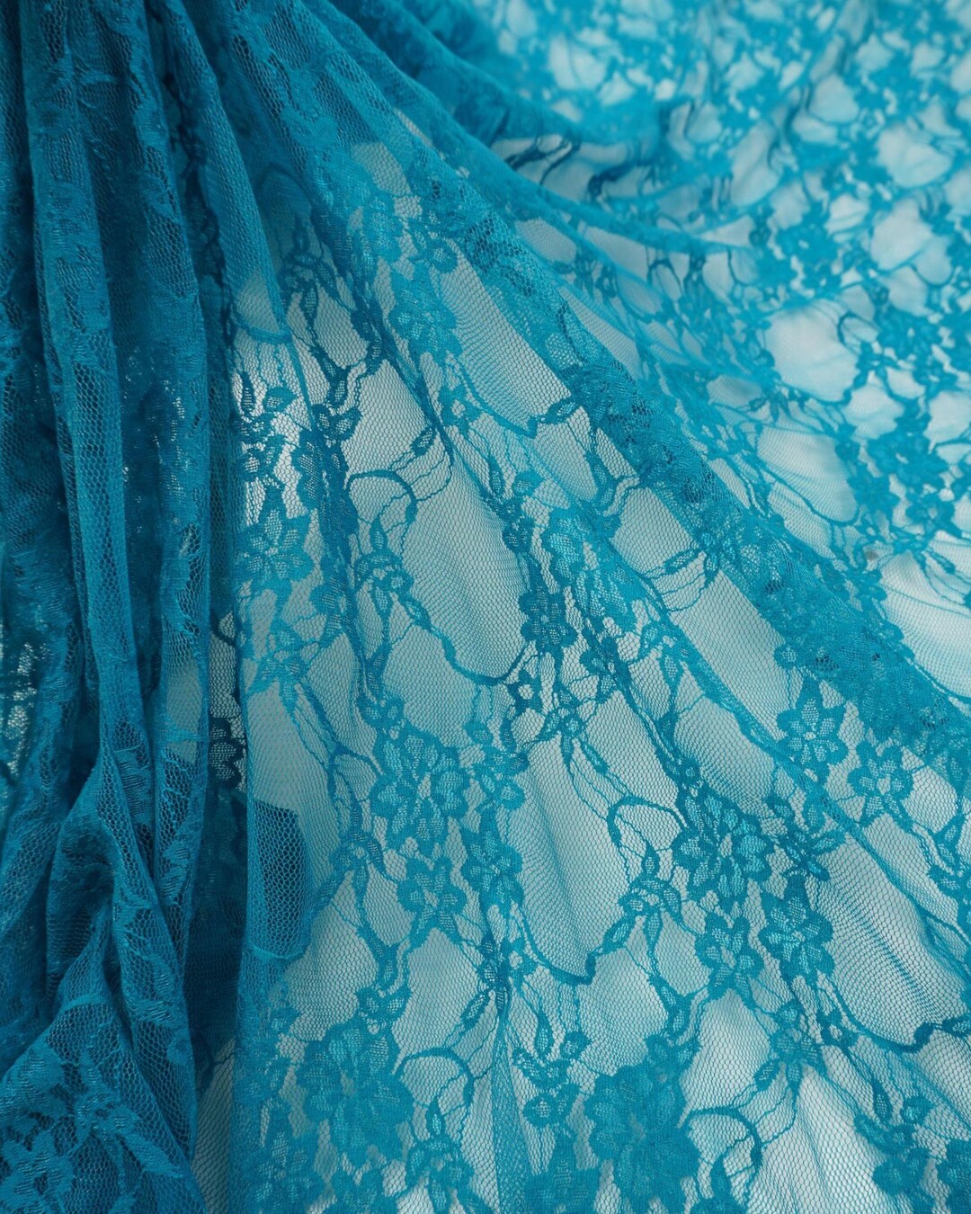 Flowing turquoise teal floral stretch lace fabric semi-transparent close-up