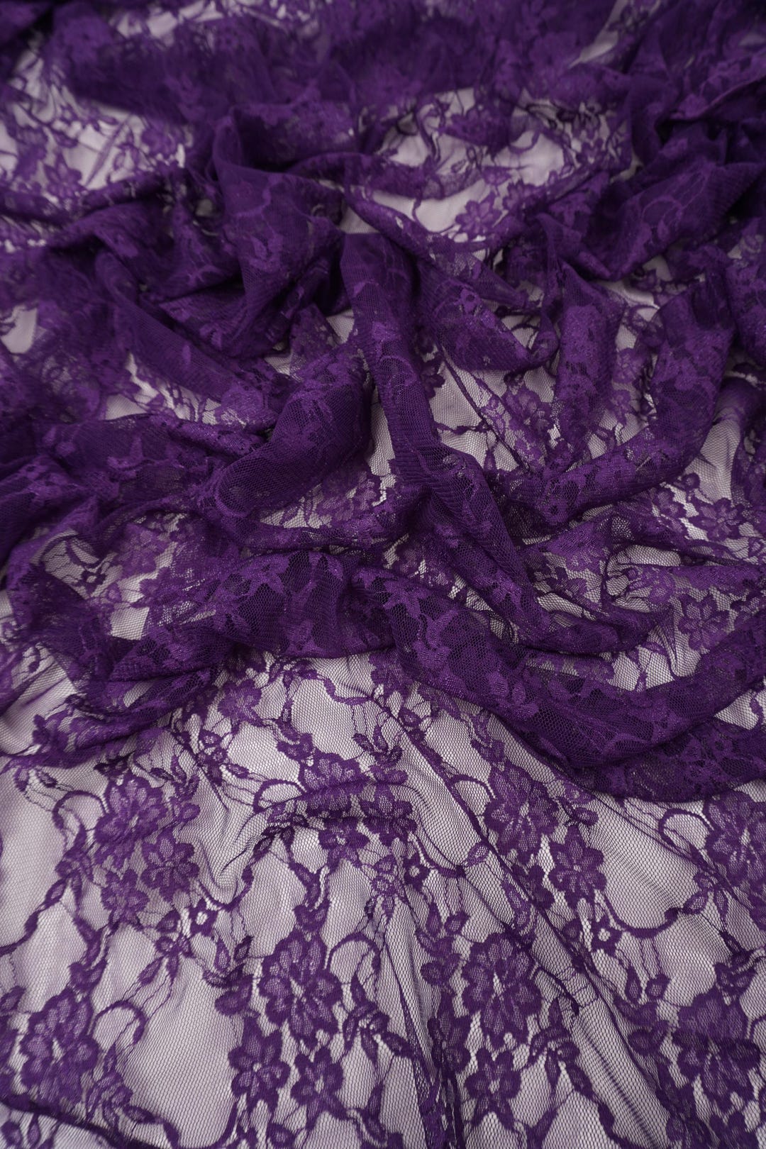 Deep purple eggplant floral lace fabric draped showing rich color and sheer texture