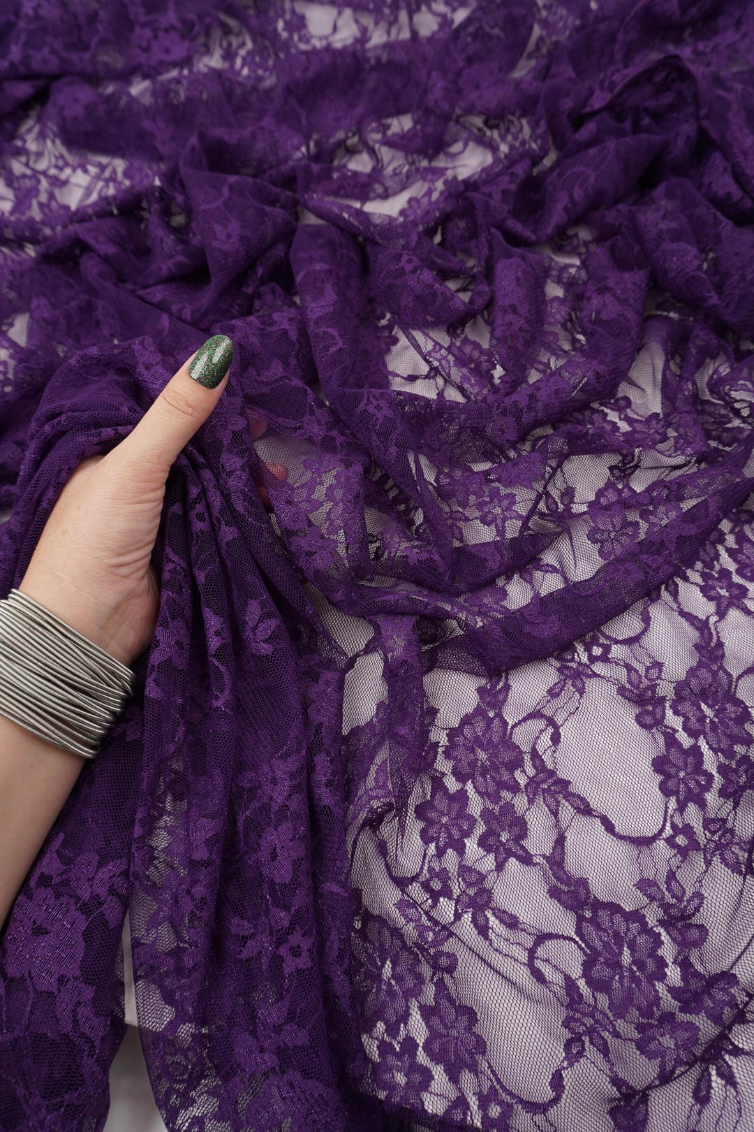Hand holding deep eggplant purple floral stretch lace fabric showing soft texture
