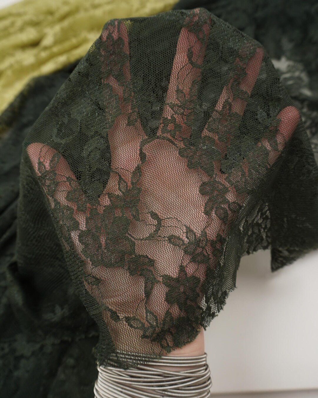 Dark hunter green floral lace fabric held up allowing light through showing pattern