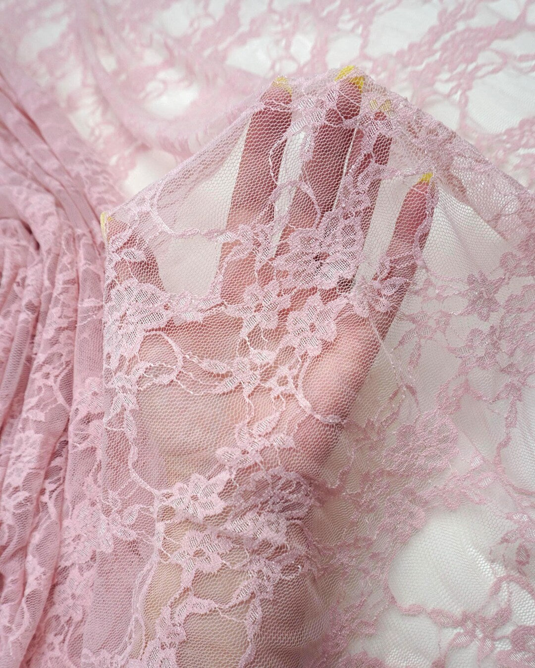 Blush dusty pink vintage floral stretch lace fabric held up showing delicate sheer pattern