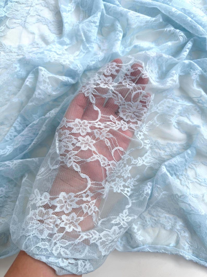 Baby Blue Floral Stretch Lace Fabric held in hand showing transparency and intricate design