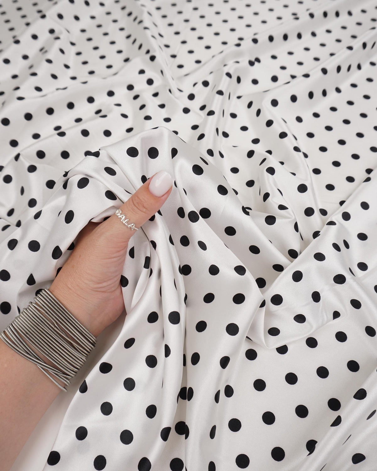 Ivory satin fabric with small black polka dots draped in soft folds