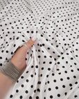 Ivory satin fabric with small black polka dots draped in soft folds