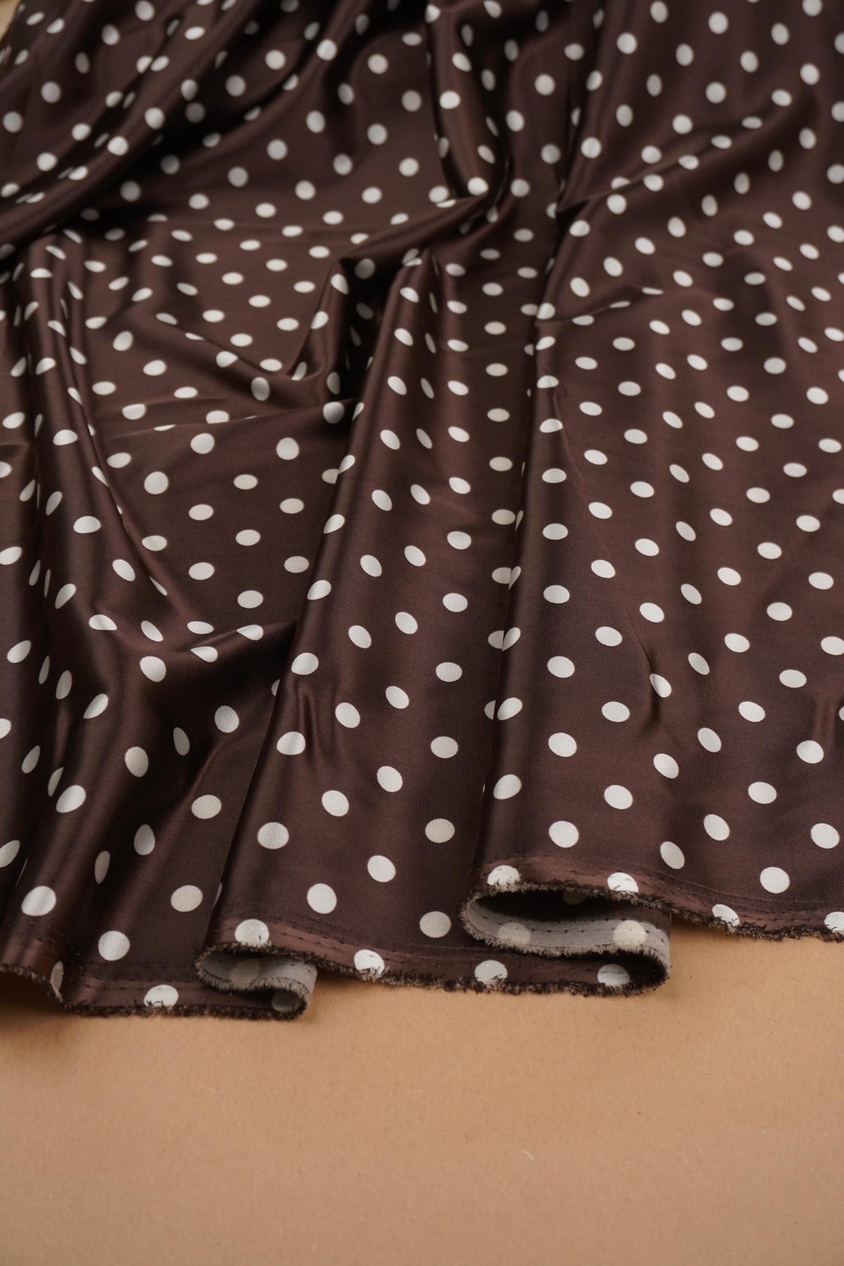 Chocolate brown and ivory polka dot stretch satin fabric draped in soft folds