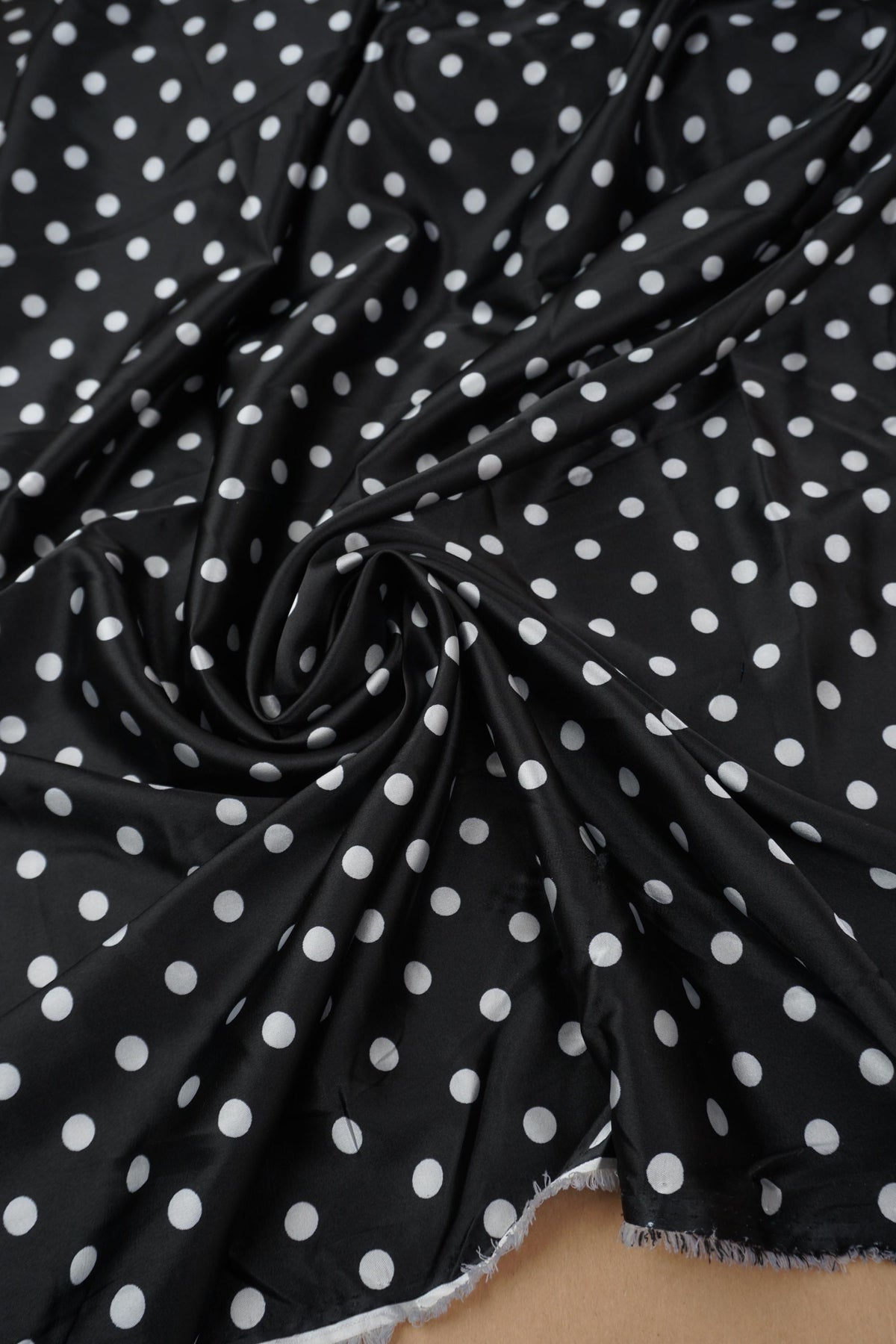 Black and white polka dot stretch satin fabric draped in soft folds