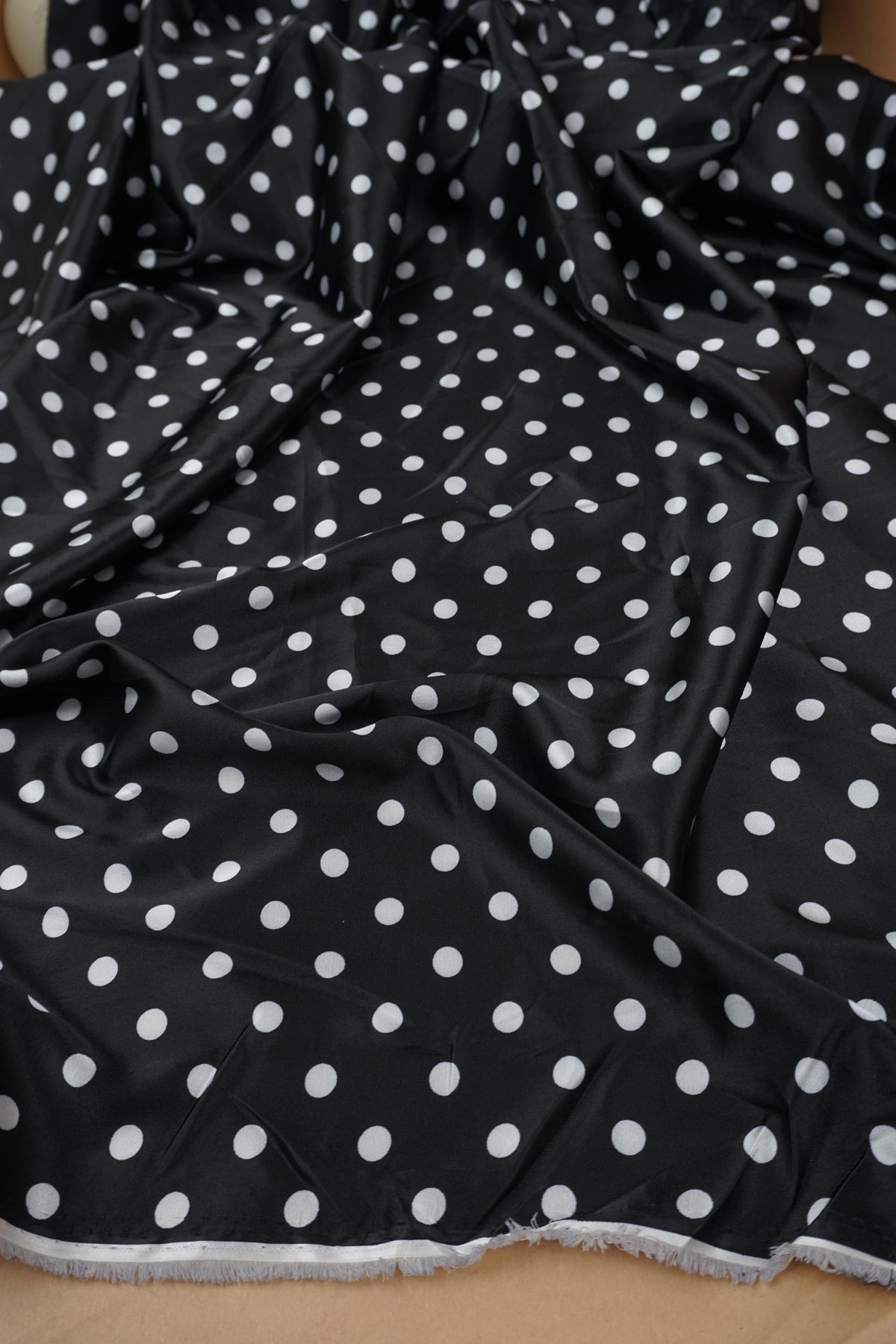 Black polka dot satin fabric showing the selvage edge